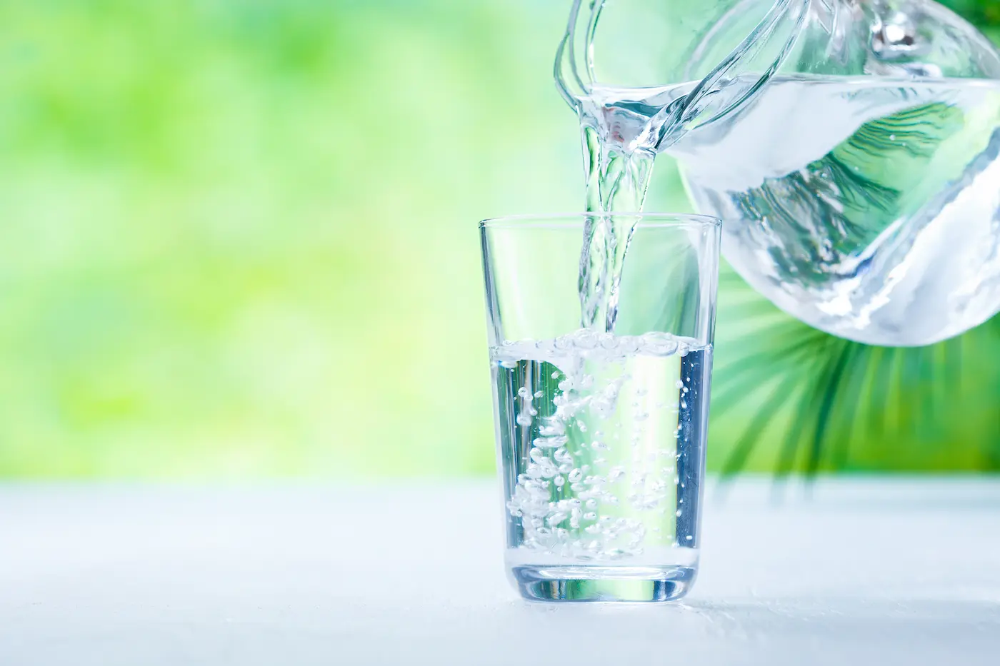 A close-up of water being poured into a clear glass sitting on a table.