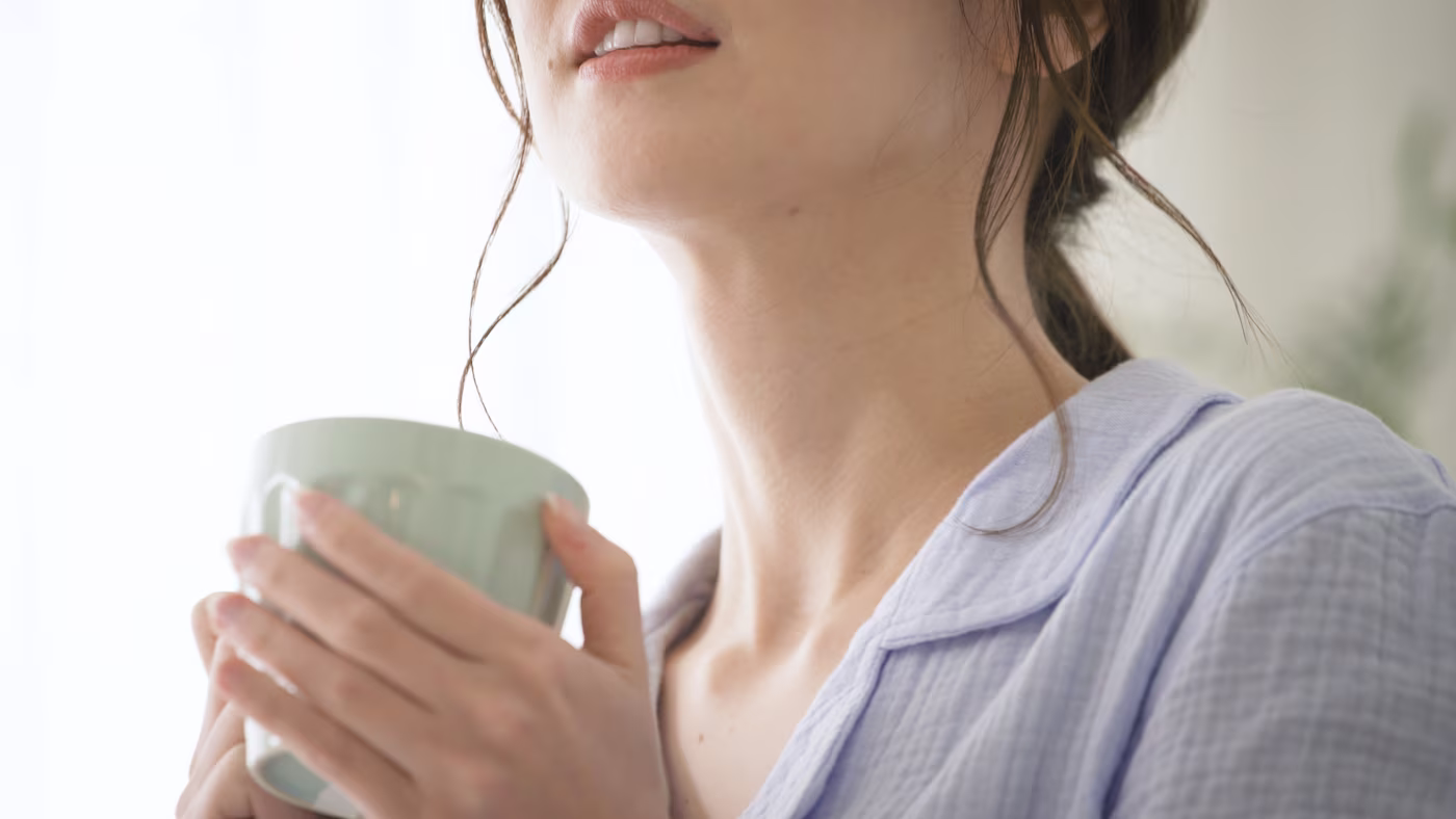 A woman wrapped in a warm pajama, holding a cozy mug with both hands.