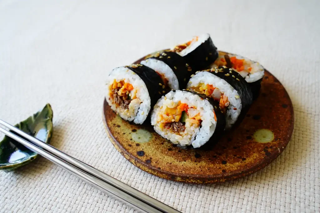 생기 넘치고 알록달록한 채소와 소고기가 듬뿍 들어간 한국식 김밥이 아름답게 담겨 있는 접시.