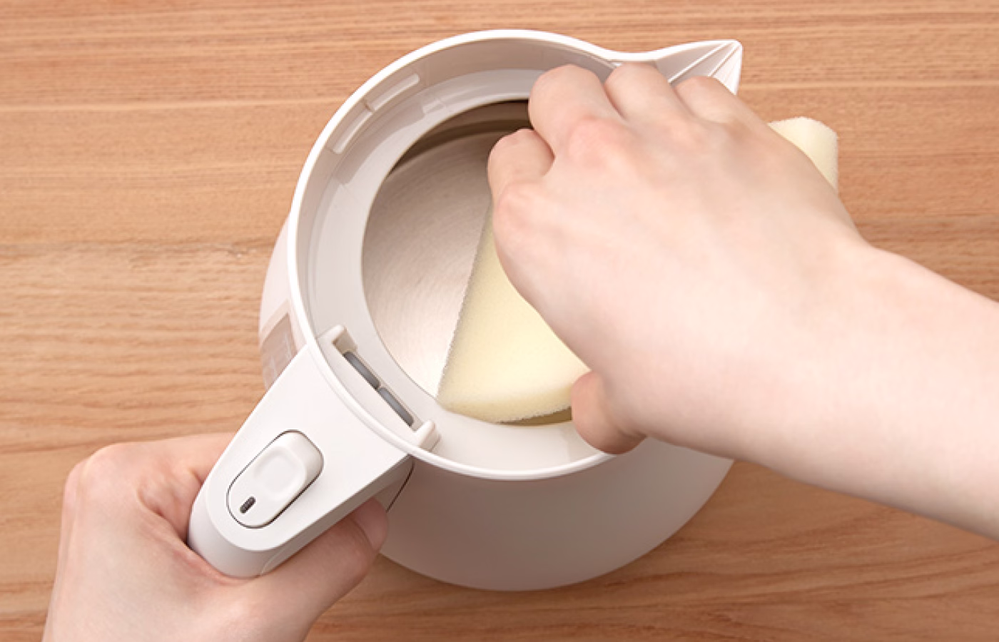Someone carefully cleaning the exterior of an electric kettle.