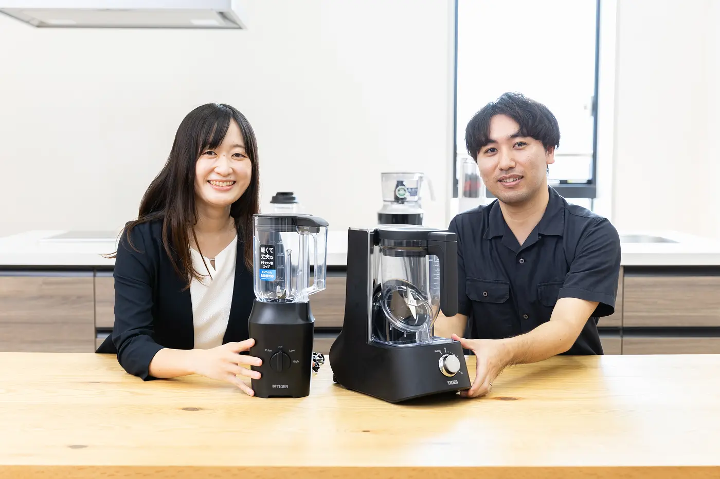 Satomi Kantani from the Product Planning Team, Solution Group, and Taiga Kamei from Product Development at Tiger Corporation, standing together with the Premium Blenders⟨TIGER EDGE⟩ models SLB-A100 and SLC-A100.