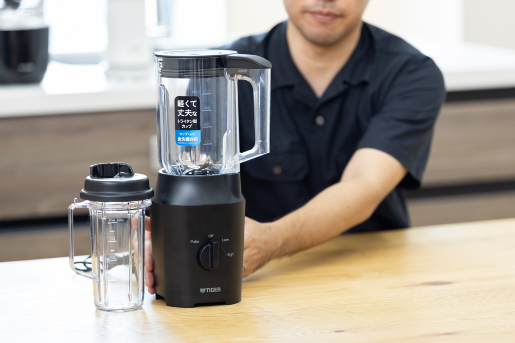 Kamei standing with the compact ⟨TIGER EDGE⟩ SLC-A100 blender and personal cup placed side by side.