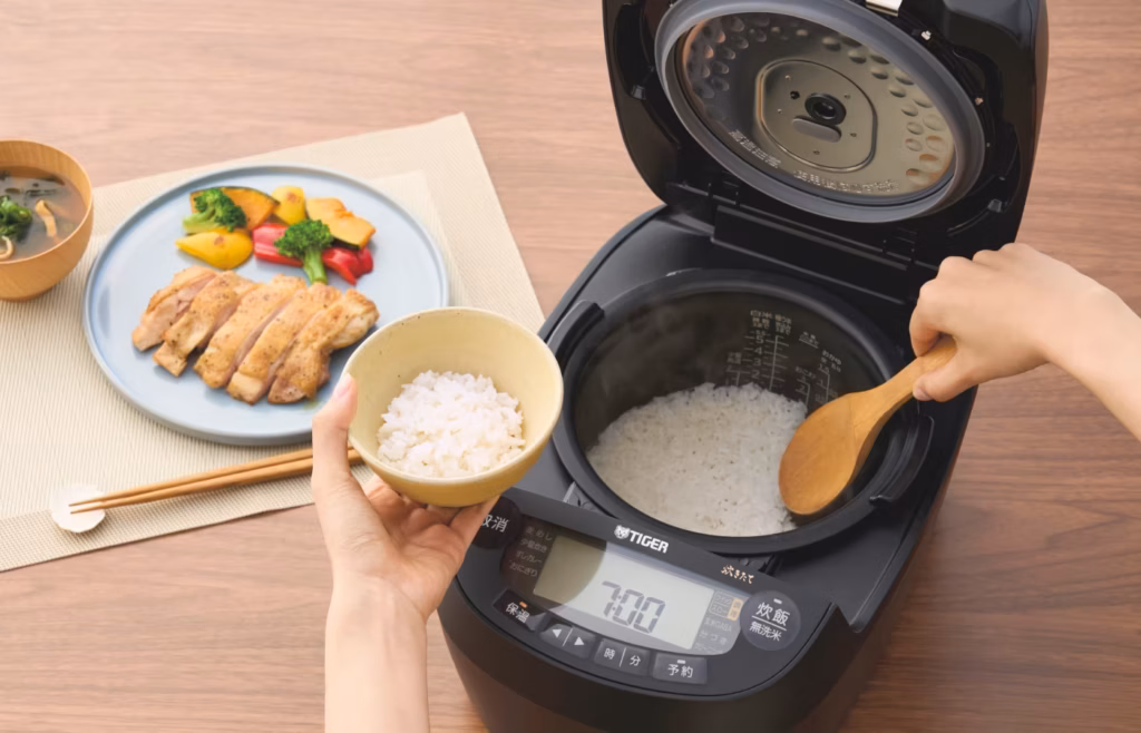 A person scooping fresh rice out of a rice cooker with a rice paddle.