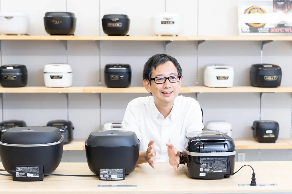Mr. Meshizuka speaking in front of three Tiger rice cookers lined up
