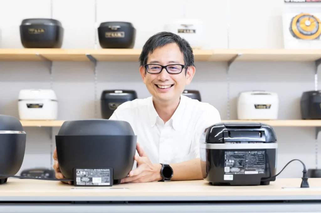 Mr.Meshiizuka speaking in front of the lined-up rice cookers
